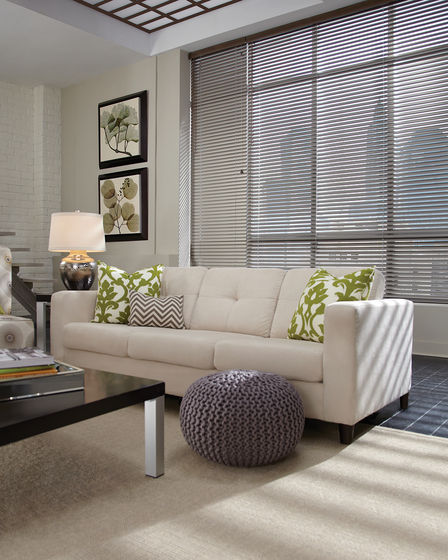 Aluminum blinds in the living room with a white couch and green pillows