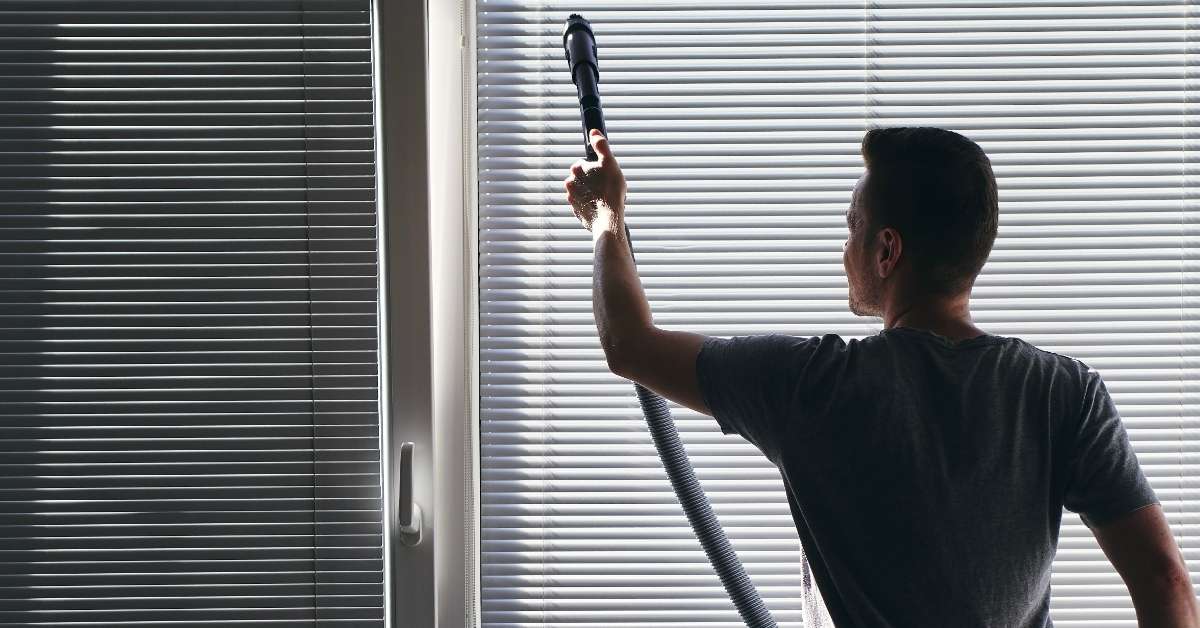 Man cleaning blinds with a vacuum cleaner